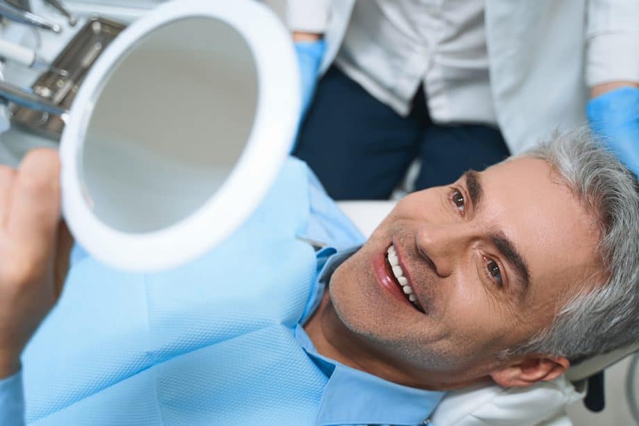 man smiling into a mirror from dentist chair