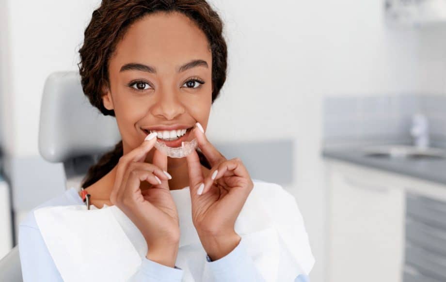 smiling woman holds Invisalign tray close to her mouth